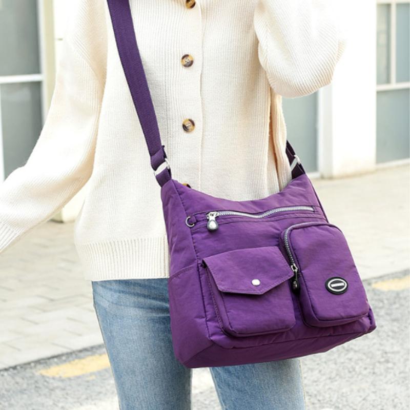 Borsa a tracolla viola da donna con tasche multiple, chiusura a zip, indossata su maglione bianco e jeans. Accessorio moda casual e pratico.