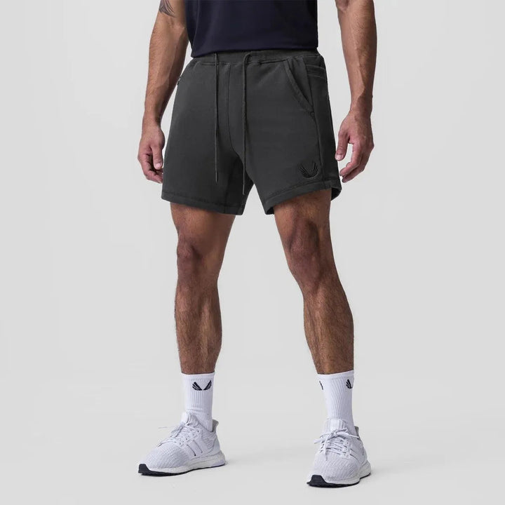 Shorts sportivi neri da uomo, con tasche e coulisse, indossati con scarpe da ginnastica bianche. Ideali per allenamento e tempo libero.
