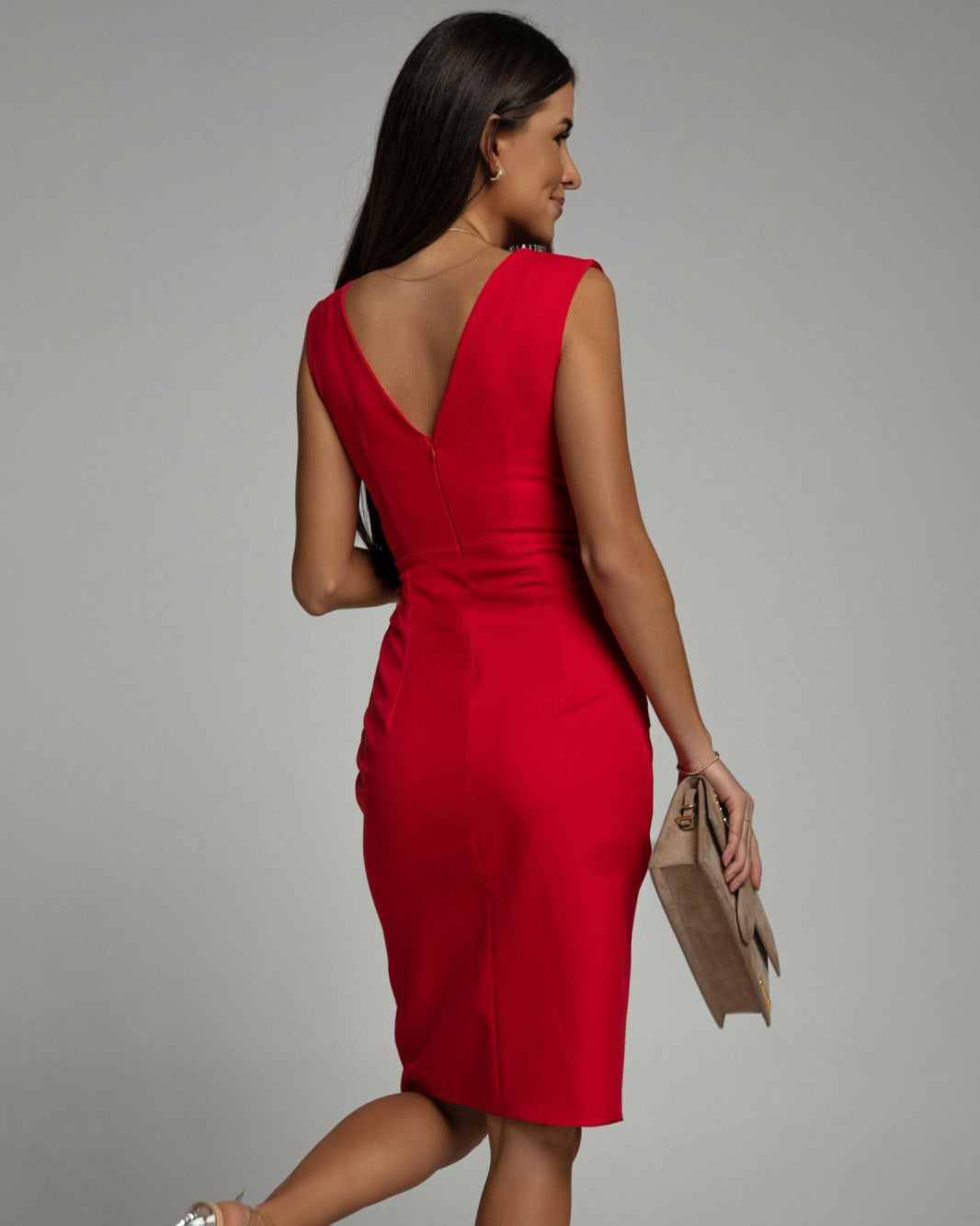 Abito rosso elegante da donna, senza maniche, con scollo a V sulla schiena. Modello aderente, perfetto per eventi serali. Accessori: borsa beige.