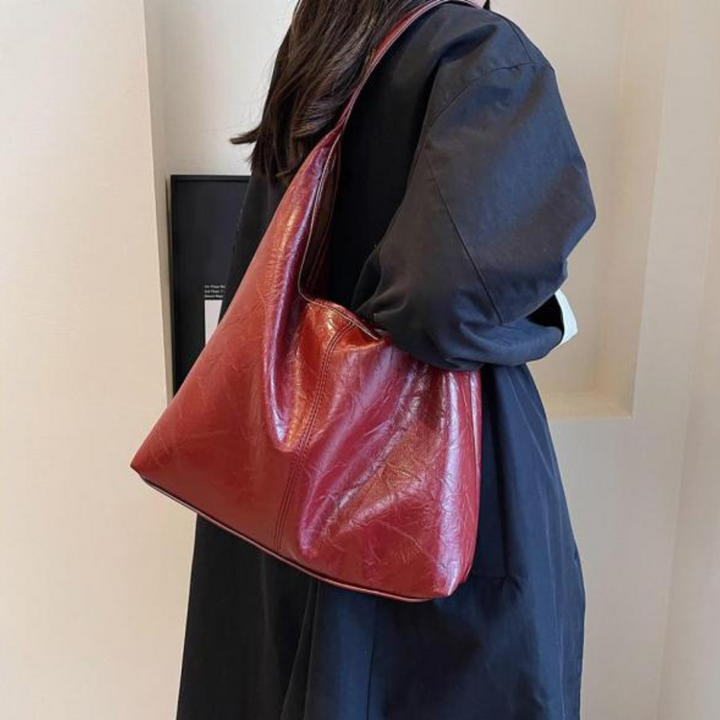 Borsa a spalla in pelle rossa lucida, indossata da una persona con cappotto nero. Accessorio moda elegante e versatile per donna.