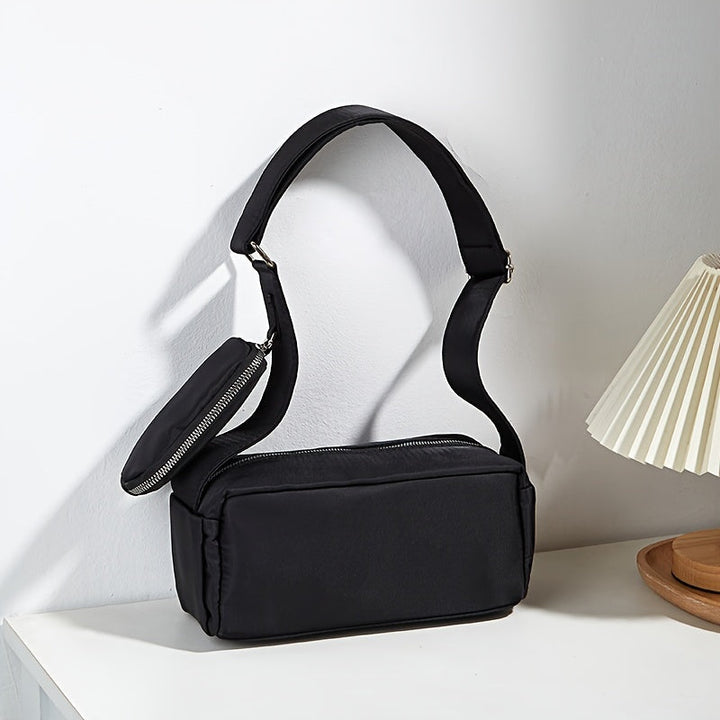 Borsa a tracolla nera elegante su tavolo bianco, design minimalista, con tasca con zip, perfetta per moda donna, accessori versatili e moderni.