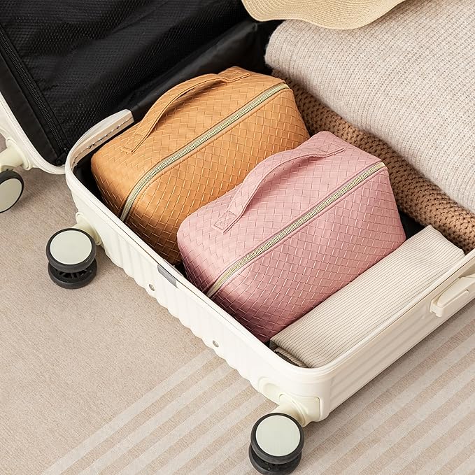 Valigia aperta con organizer da viaggio intrecciati in pelle, colori rosa e beige, su sfondo beige. Perfetta per viaggi organizzati e moda.