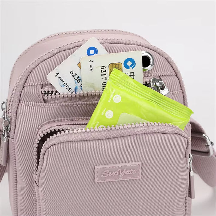 Zaino rosa compatto con tasche multiple, contenente carte di credito, smartphone e salviettine. Accessorio moda pratico e versatile per donna.