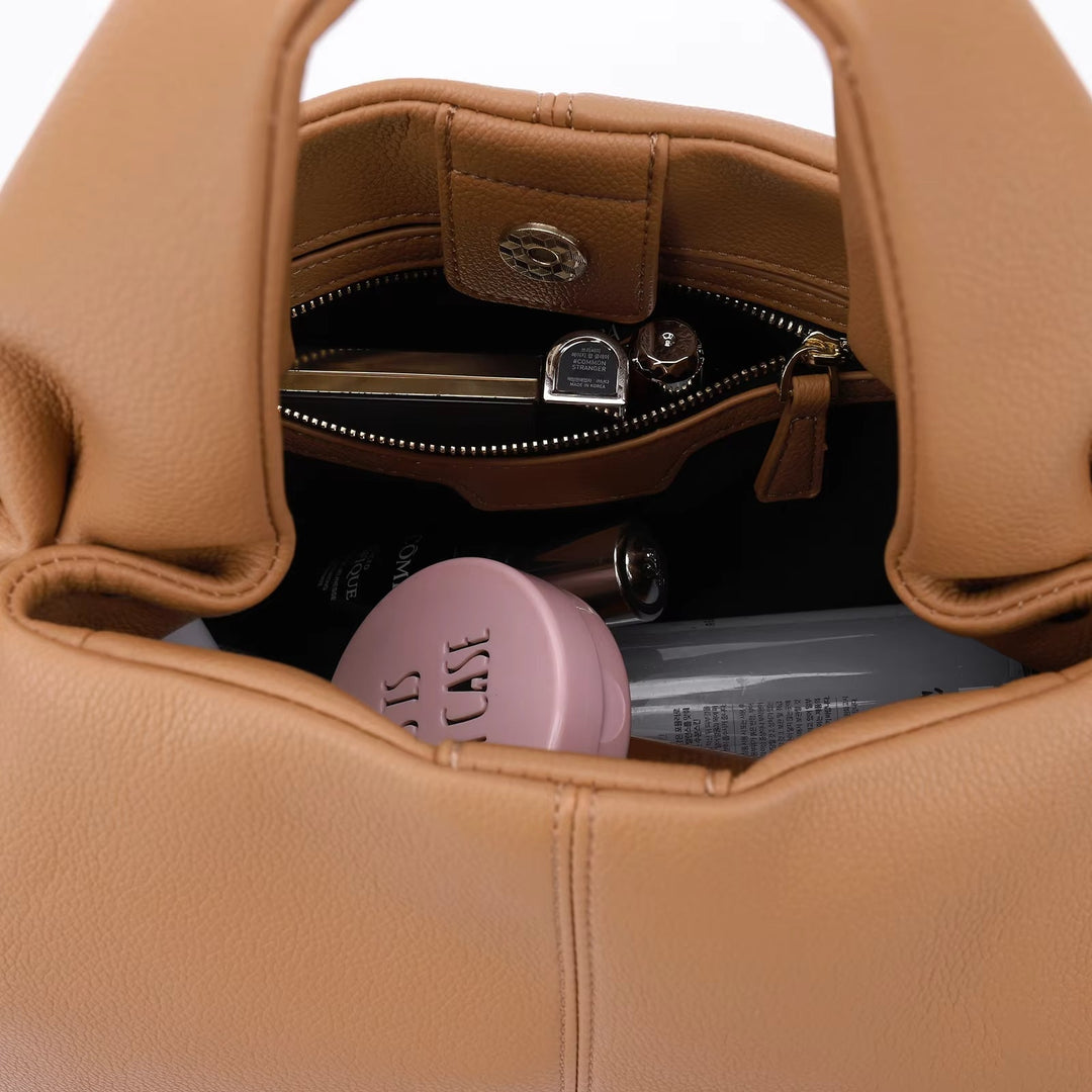 Borsa in pelle marrone aperta, contenente rossetto, specchietto, crema rosa e altri accessori. Elegante e spaziosa, ideale per l'uso quotidiano.