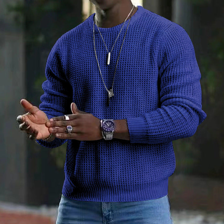 Maglione blu uomo, lavorato a maglia, indossato con jeans. Accessori: orologio, collane, anelli. Moda casual autunno/inverno.