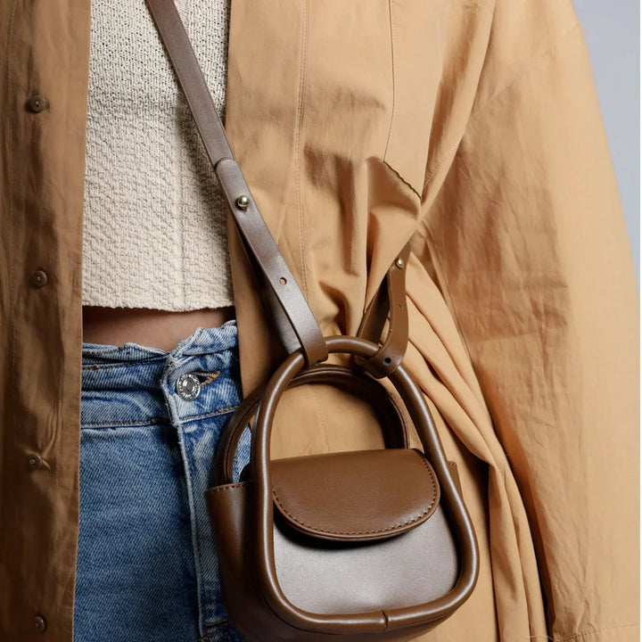 Borsa a tracolla marrone in pelle, design moderno, indossata su giacca beige e jeans. Accessorio moda donna, stile casual chic.