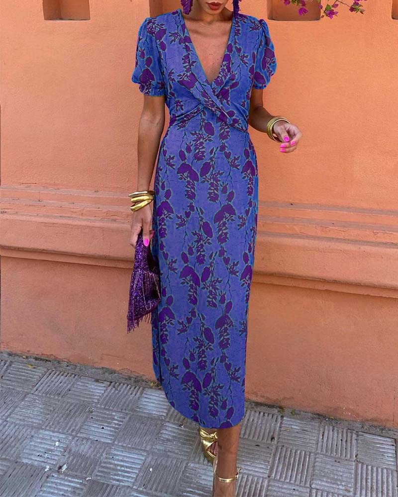 Abito lungo floreale blu e viola con scollo a V, maniche corte e accessori dorati. Perfetto per moda estiva elegante e occasioni speciali.