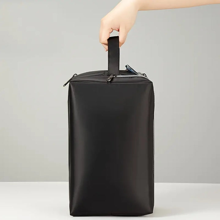Mano che tiene una borsa da viaggio nera impermeabile con cerniera, design minimalista, ideale per organizzare accessori e articoli da toeletta.