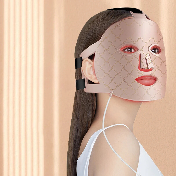 Donna con maschera LED per terapia della pelle, design elegante, colore rosa, utilizzata per trattamenti anti-età e cura del viso, sfondo beige.