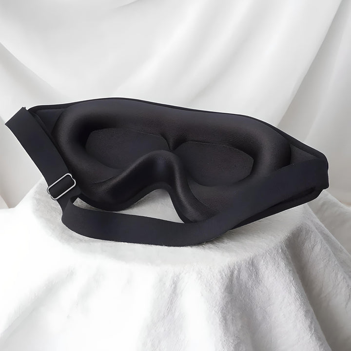 Maschera per dormire nera in memory foam su sfondo bianco, design ergonomico, cinturino regolabile, accessorio per il sonno, comfort notturno.