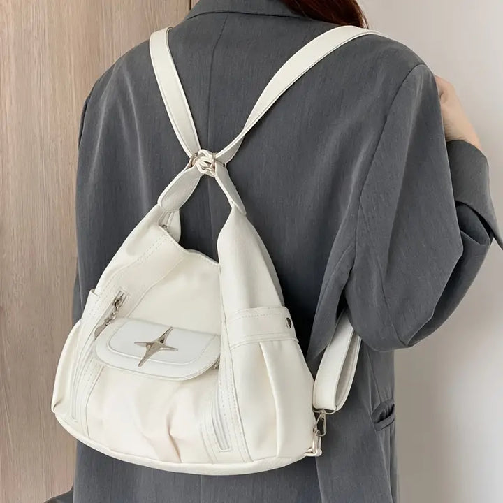 Zaino bianco in pelle su donna con giacca grigia, design moderno, tasca frontale con zip, ideale per moda urbana e viaggi.