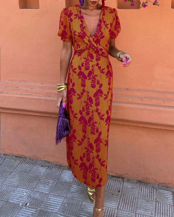 Abito lungo floreale arancione e rosso, maniche corte, scollo a V, accessori oro, borsa viola, sandali dorati, moda donna elegante estiva.