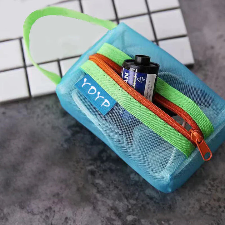 Custodia trasparente blu con cerniera arancione e verde, contenente una batteria. Design compatto, ideale per organizzare piccoli accessori.