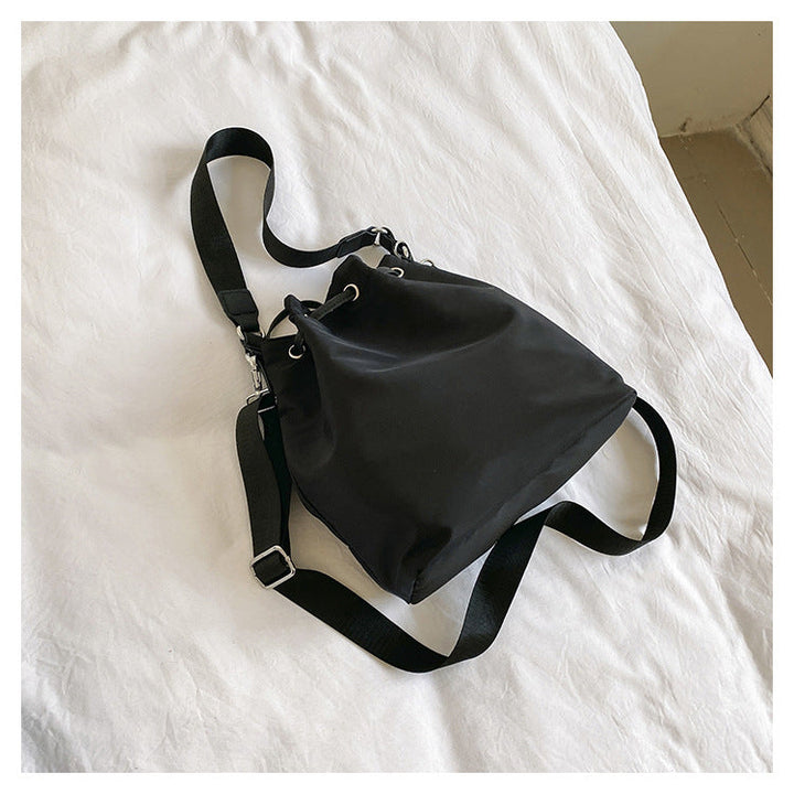 Borsa a tracolla nera su letto bianco, design minimalista, tessuto resistente, ideale per moda casual e quotidiana. Accessorio versatile ed elegante.