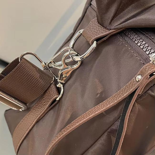 Borsa a tracolla marrone in tessuto resistente con cerniera e moschettone in metallo argentato, ideale per viaggi e uso quotidiano.