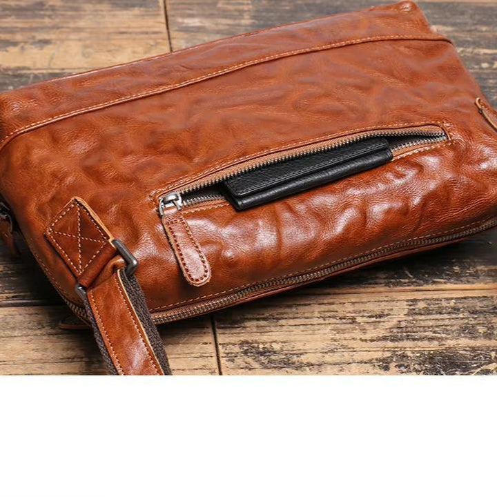 Borsa a tracolla in pelle marrone su tavolo in legno, con cerniera frontale e tracolla regolabile. Accessorio moda elegante e pratico.