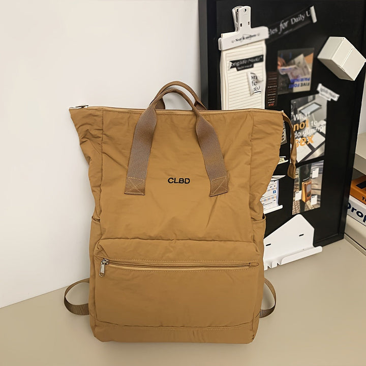 Zaino beige CLBD in tessuto resistente, con manici in pelle e tasca frontale con zip, posizionato su scrivania moderna.