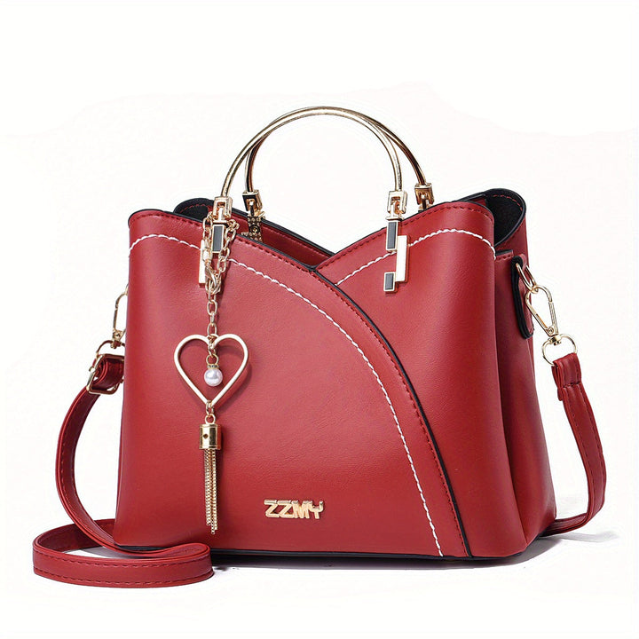 Borsa a mano rossa in pelle con dettagli dorati, tracolla regolabile e ciondolo a cuore. Design elegante e moderno, perfetta per ogni occasione.