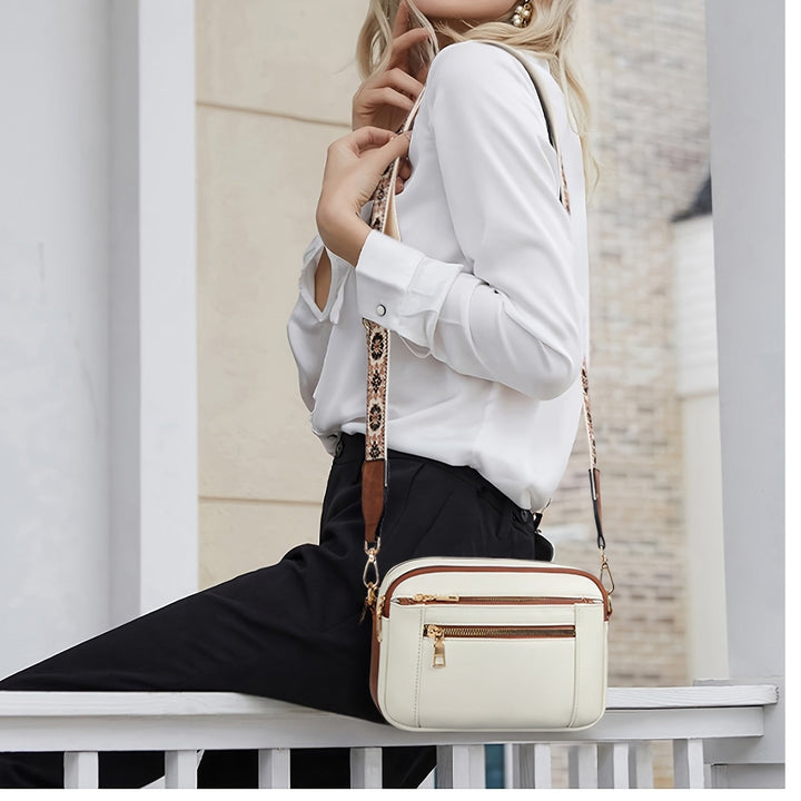 Donna con borsa a tracolla bianca in pelle, dettagli dorati, indossa camicia bianca e pantaloni neri. Accessorio moda elegante e versatile.