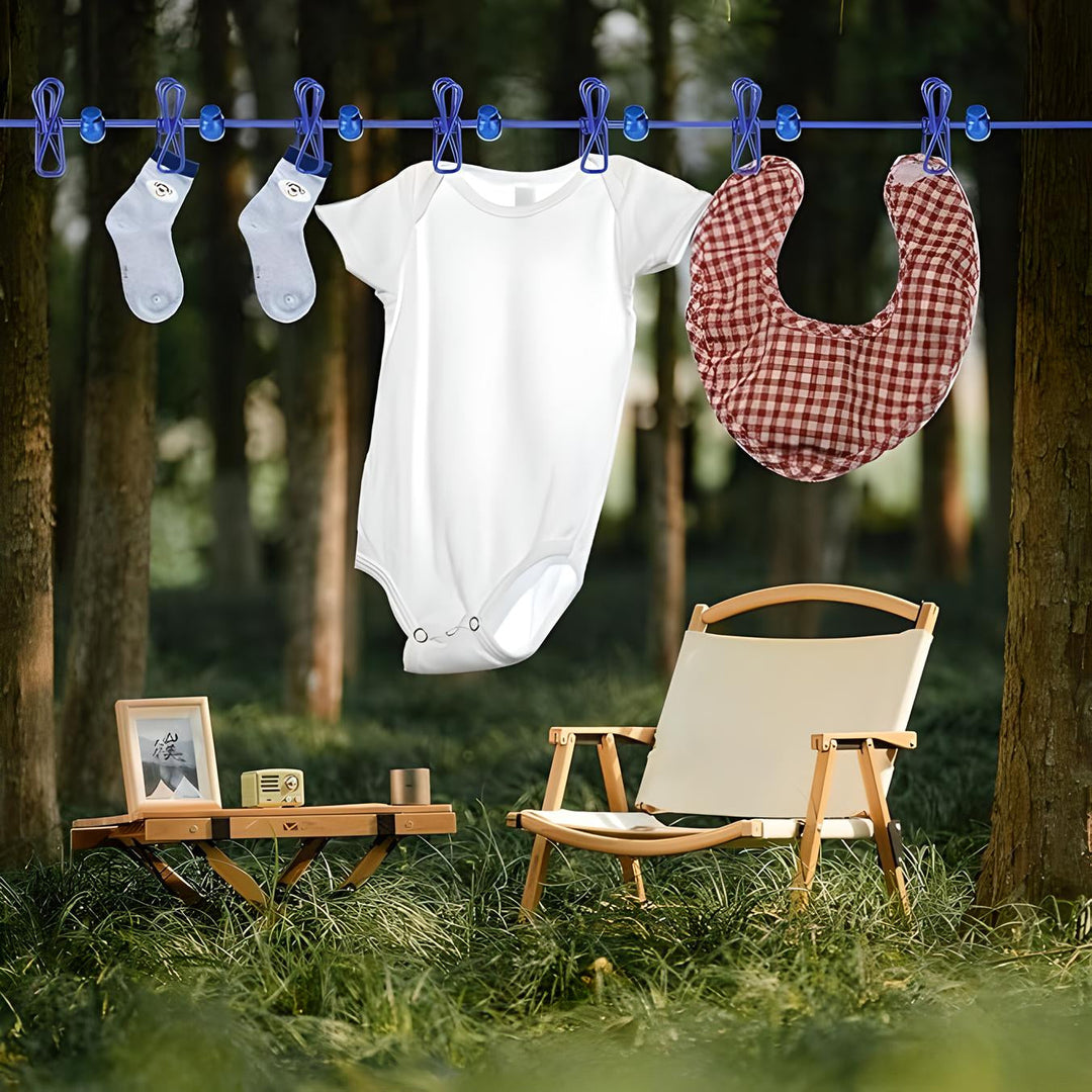 Body neonato bianco, calzini e bavaglino a quadri appesi su filo in giardino. Sedia e tavolino in legno su prato verde. Abbigliamento bambino estivo.