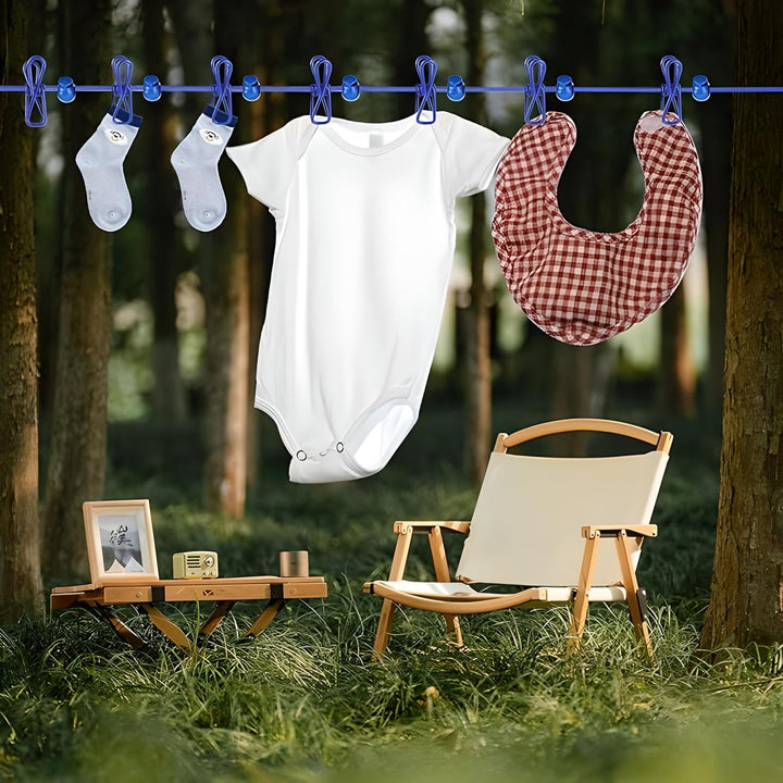 Body neonato bianco, calzini e bavaglino a quadri appesi su filo in giardino. Sedia e tavolino in legno su prato verde. Abbigliamento bambino estivo.