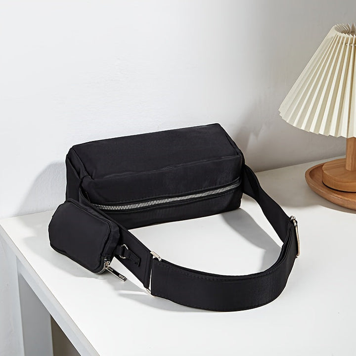 Marsupio nero elegante su tavolo bianco, con cerniera argentata e tasca aggiuntiva. Accessorio moda unisex, ideale per viaggi e uso quotidiano.