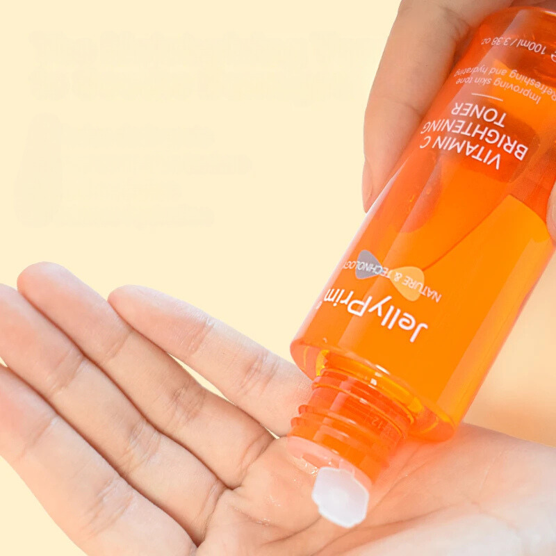 Mano che versa tonico illuminante alla vitamina C Jelly Prim su palmo. Flacone arancione, skincare viso, idratazione, trattamento anti-età.