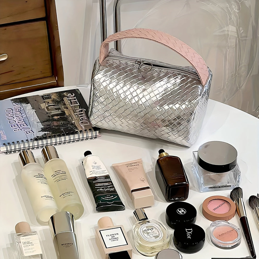 Borsa cosmetica intrecciata argento su tavolo con prodotti di bellezza: creme, profumi, trucco. Accessori moda e bellezza, stile elegante.