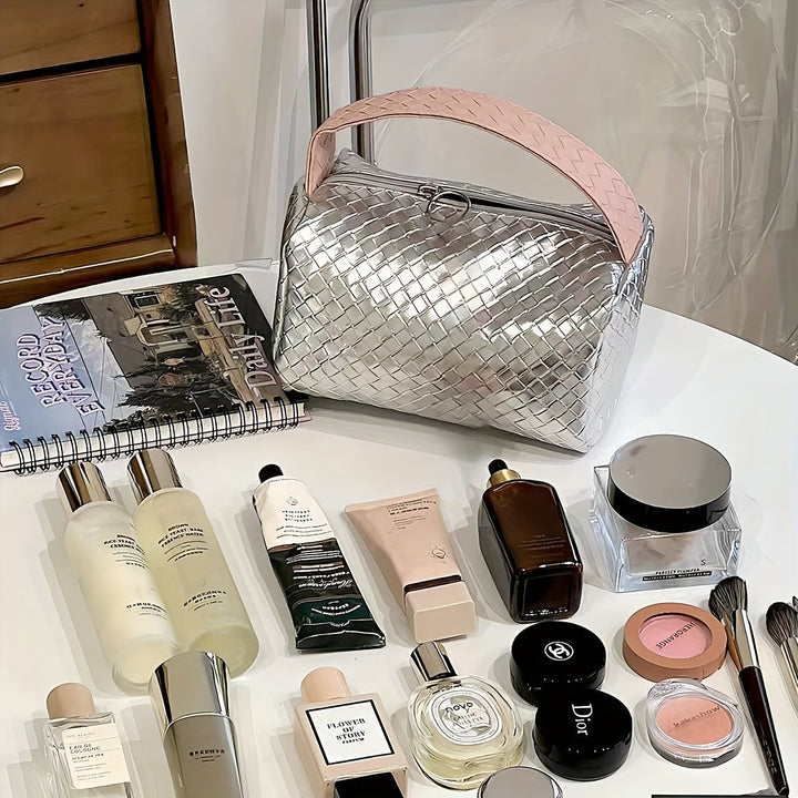 Borsa cosmetica intrecciata argento su tavolo con prodotti di bellezza: creme, profumi, trucco. Accessori moda e bellezza, stile elegante.
