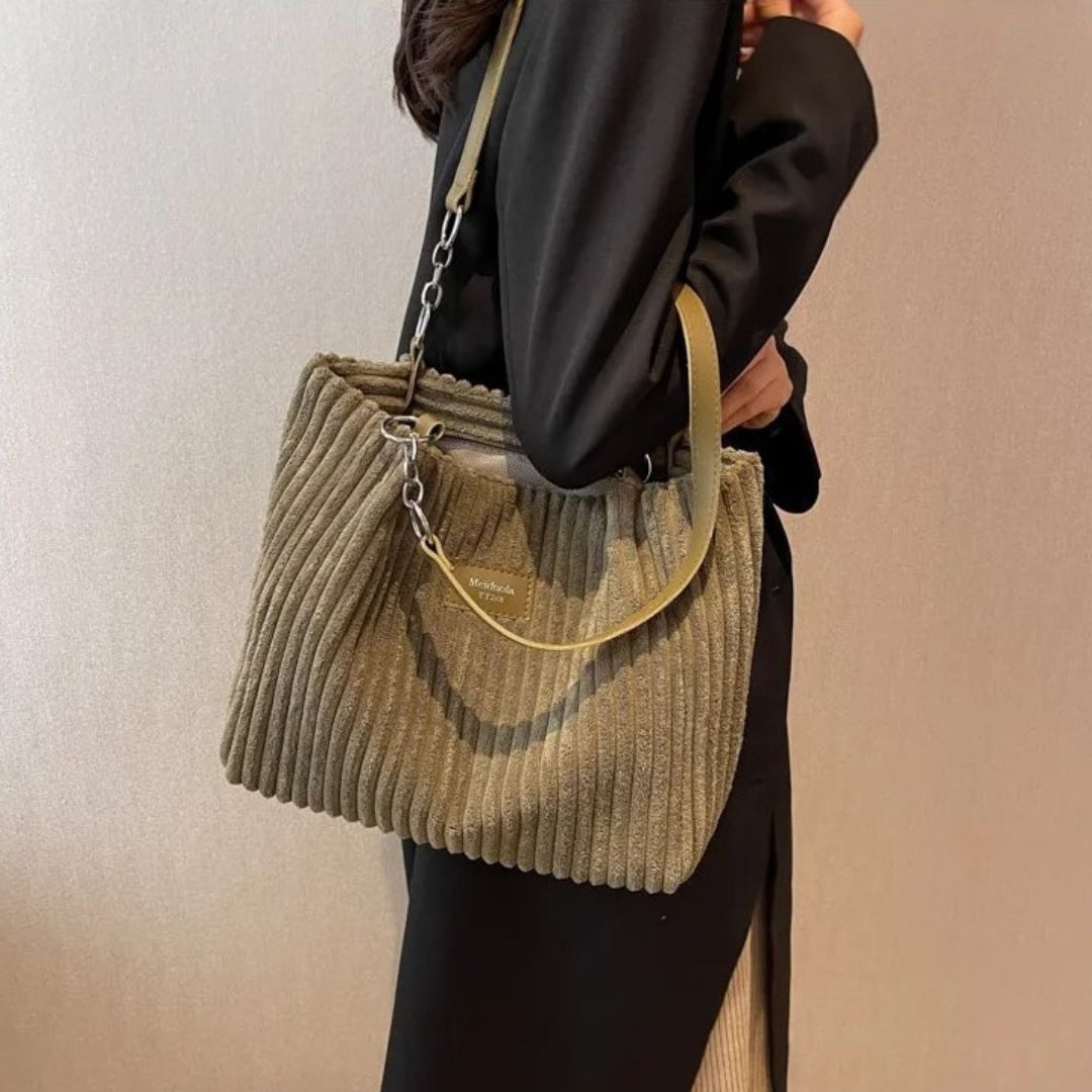 Donna con borsa a tracolla verde oliva in velluto a coste, dettagli in metallo, indossa abito nero elegante. Accessorio moda autunno inverno.