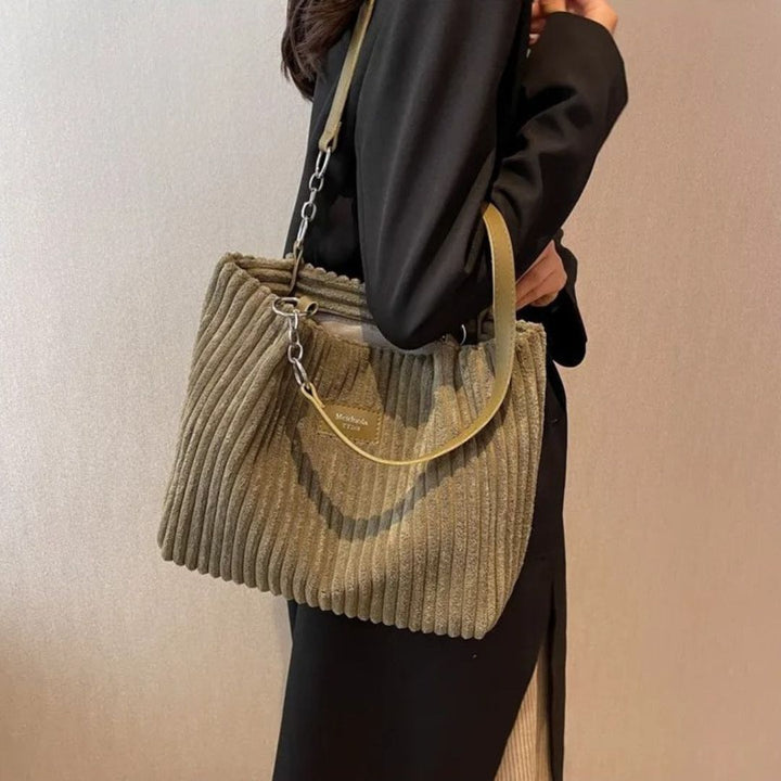 Donna con borsa a tracolla verde oliva in velluto a coste, dettagli in metallo, indossa abito nero elegante. Accessorio moda autunno inverno.