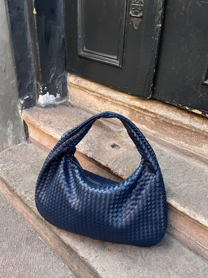 Borsa a spalla intrecciata blu scuro su gradini di pietra, design elegante e moderno, accessorio moda donna, perfetto per look casual e chic.