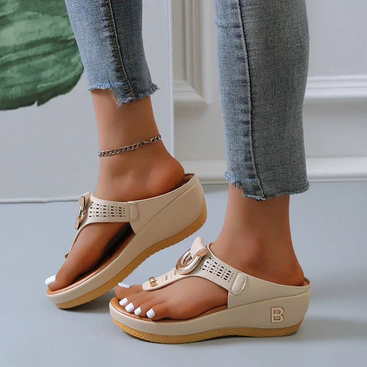 Sandali beige con zeppa, cinturino regolabile e dettagli traforati, indossati con jeans aderenti. Scarpe estive eleganti e comode per donna.