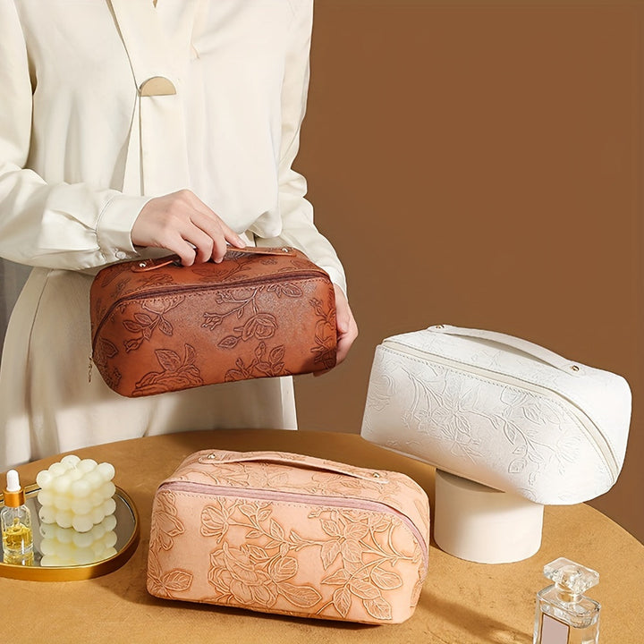Donna con borsa da toilette in pelle marrone con motivo floreale, affiancata da borse simili in bianco e beige. Accessori eleganti per il viaggio.