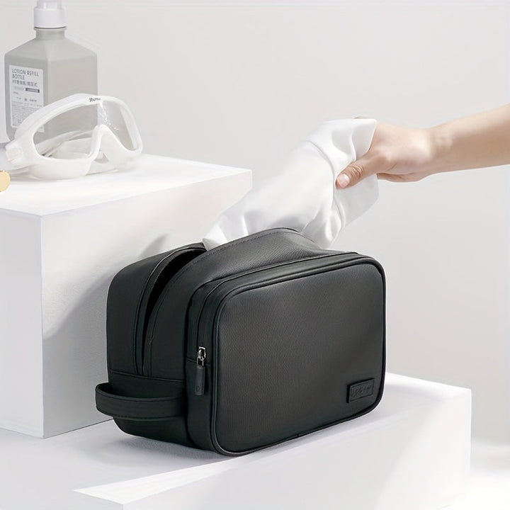 Borsa da toilette nera in pelle, elegante e spaziosa, con cerniera, ideale per viaggi. Mano che inserisce un asciugamano bianco. Accessori bagno moderni.
