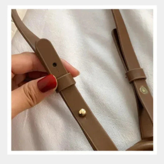 Cintura in pelle marrone con fibbia regolabile, dettaglio di chiusura a vite dorata, mano con smalto rosso. Accessorio moda elegante.