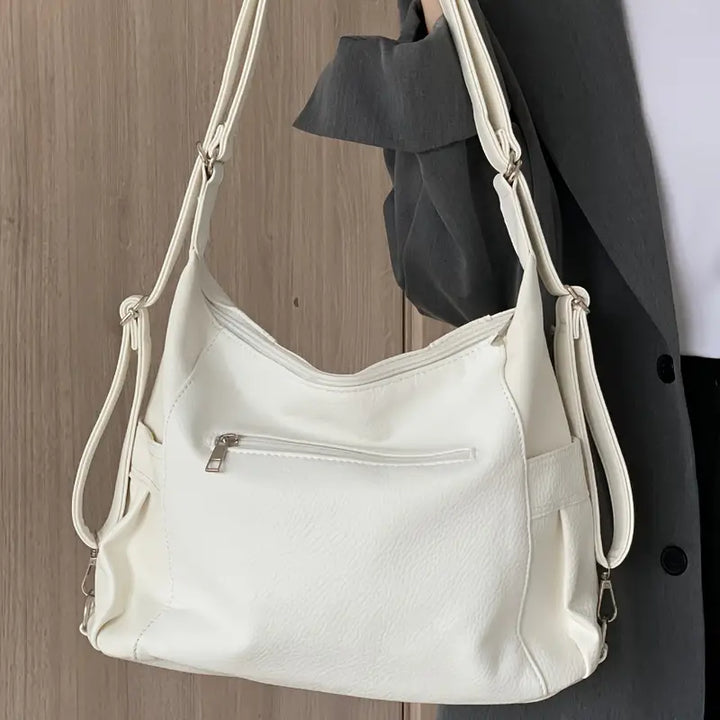 Borsa a tracolla bianca in pelle sintetica, con tasca frontale con zip, indossata da una persona in giacca grigia. Accessorio moda elegante.
