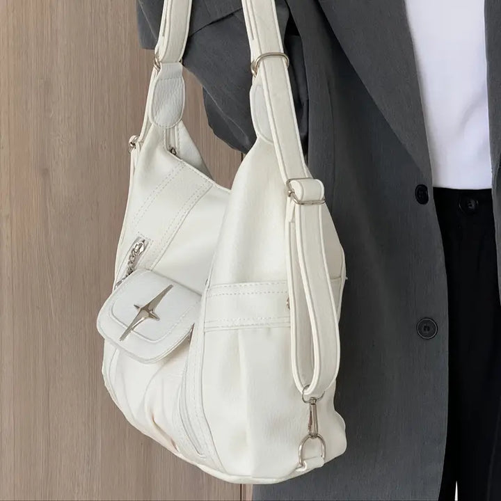 Borsa a tracolla bianca in pelle, design elegante con tasca frontale e chiusura a zip, indossata su giacca grigia. Accessorio moda donna.