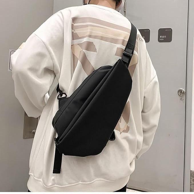 Zaino a tracolla nero unisex, indossato su felpa bianca. Design moderno, ideale per viaggi e uso quotidiano. Accessorio moda versatile e pratico.