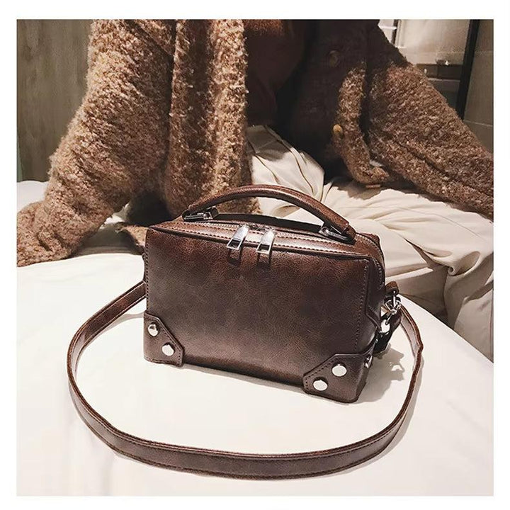 Borsa a tracolla in pelle marrone su letto, design rettangolare con manico superiore e dettagli metallici. Accessorio moda elegante per donna.