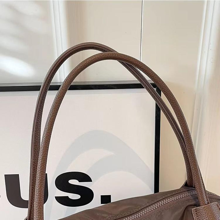 Borsa a spalla in pelle marrone con manici doppi, design elegante e moderno, ideale per moda donna. Sfondo bianco con cornice nera.