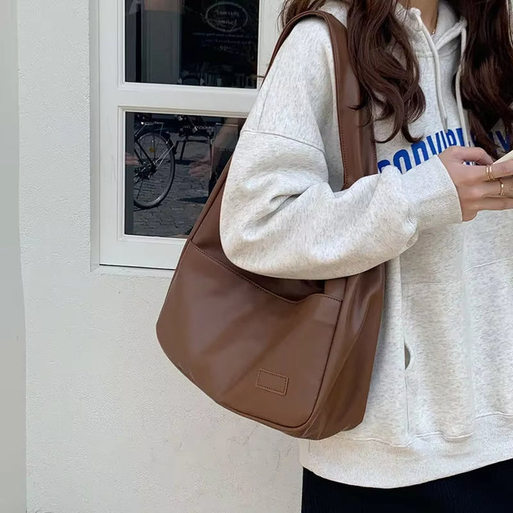 Donna con felpa grigia e borsa a tracolla marrone in pelle, stile casual. Accessorio moda femminile, ideale per look quotidiani e urbani.