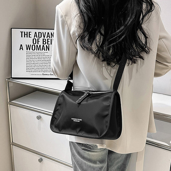 Donna con borsa a tracolla nera in nylon, indossa giacca bianca. Design moderno, ideale per moda urbana. Sfondo con poster motivazionale.