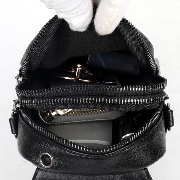 Zaino in pelle nera aperto, mostra scomparti con cerniere, chiavi e accessori all'interno. Design elegante, ideale per moda e praticità quotidiana.