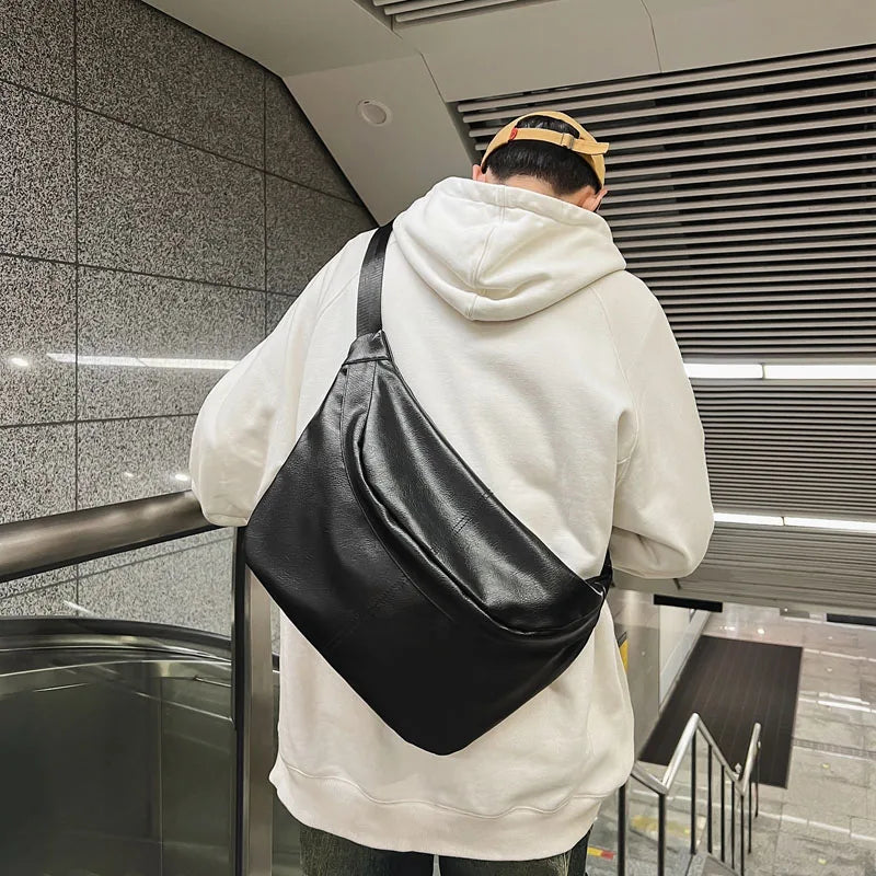 Uomo con felpa bianca e cappellino beige indossa borsa a tracolla nera in pelle, stile urbano, su scala mobile in metropolitana moderna.