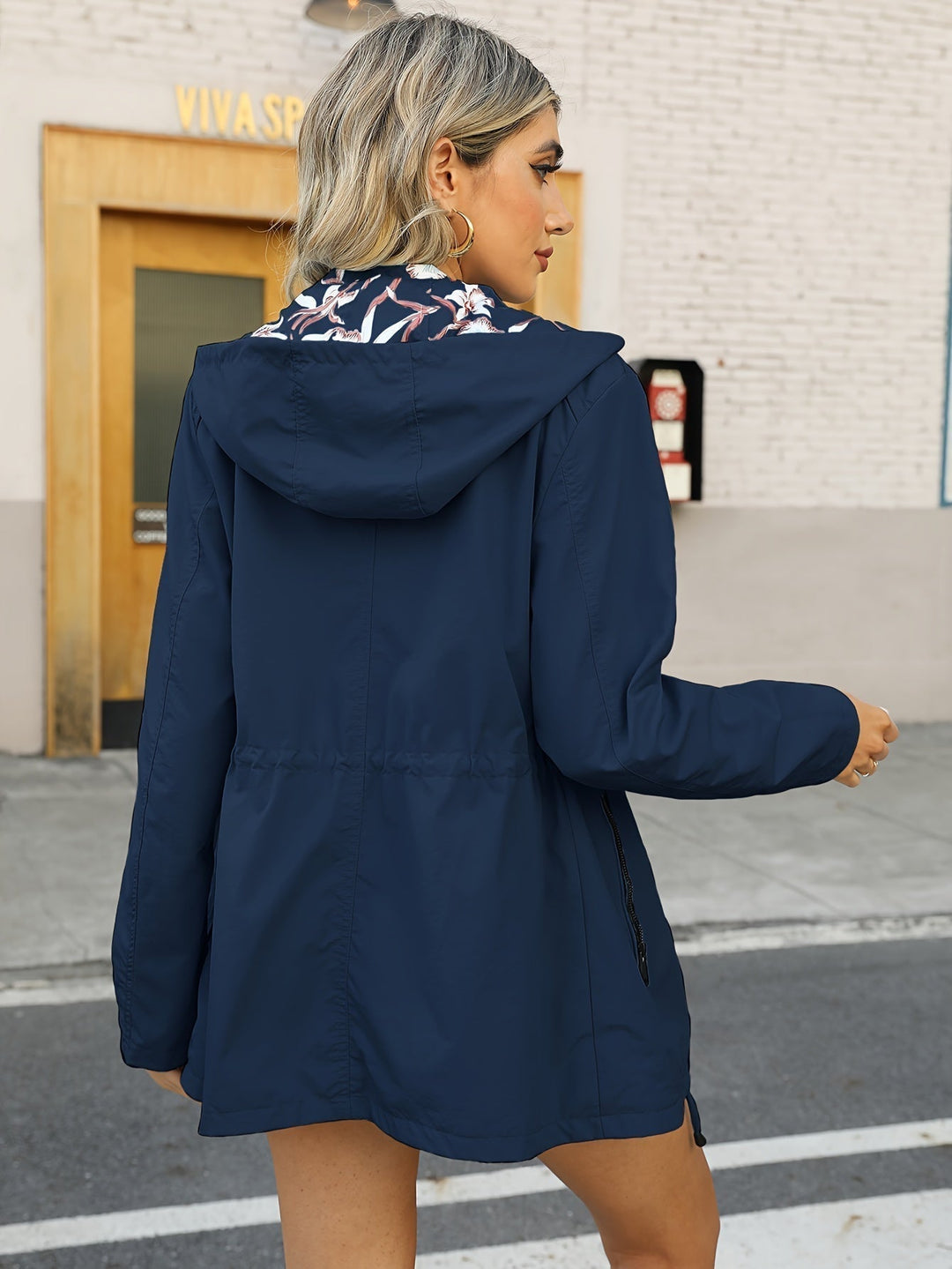 Donna con giacca a vento blu scuro, cappuccio e dettagli floreali, cammina in città. Moda autunnale, abbigliamento casual femminile.