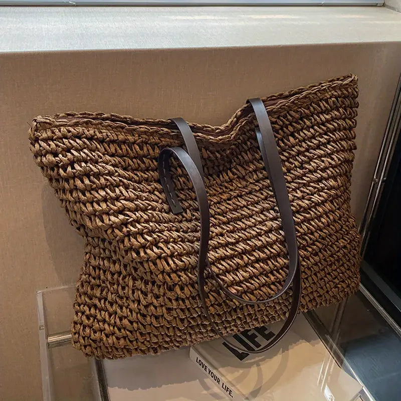 Borsa tote in paglia intrecciata con manici in pelle nera, design elegante e spazioso, perfetta per shopping e uso quotidiano.
