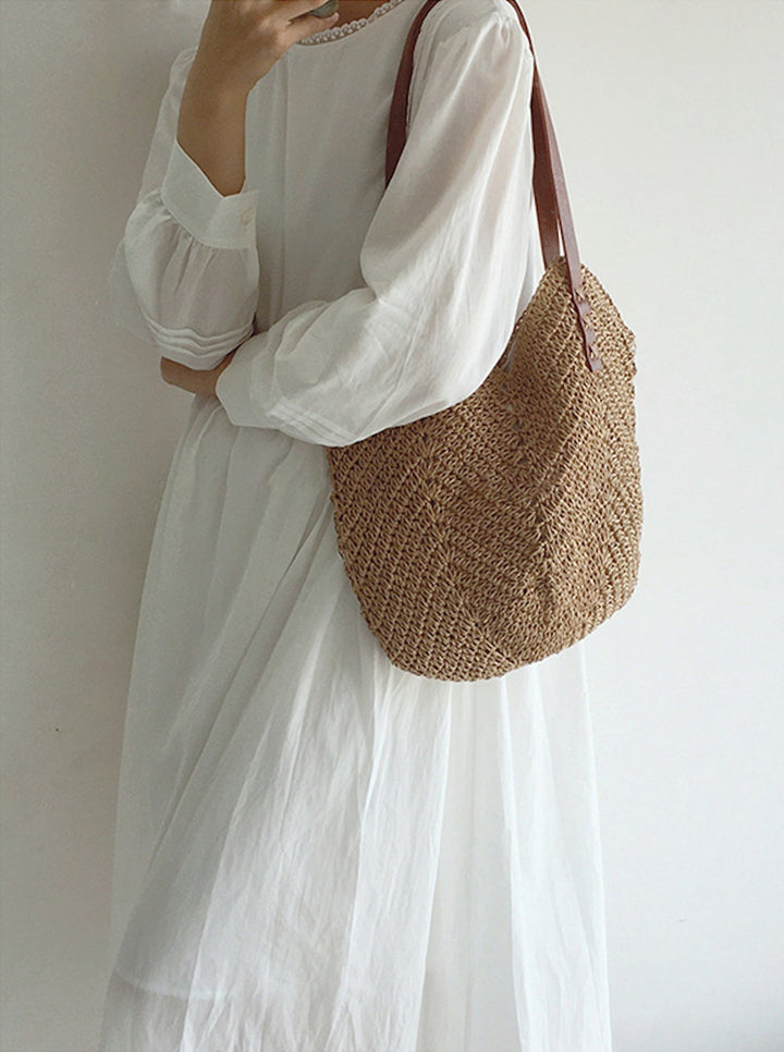 Donna con abito bianco lungo e borsa a tracolla in paglia intrecciata. Moda estiva, accessori eleganti, stile casual chic.