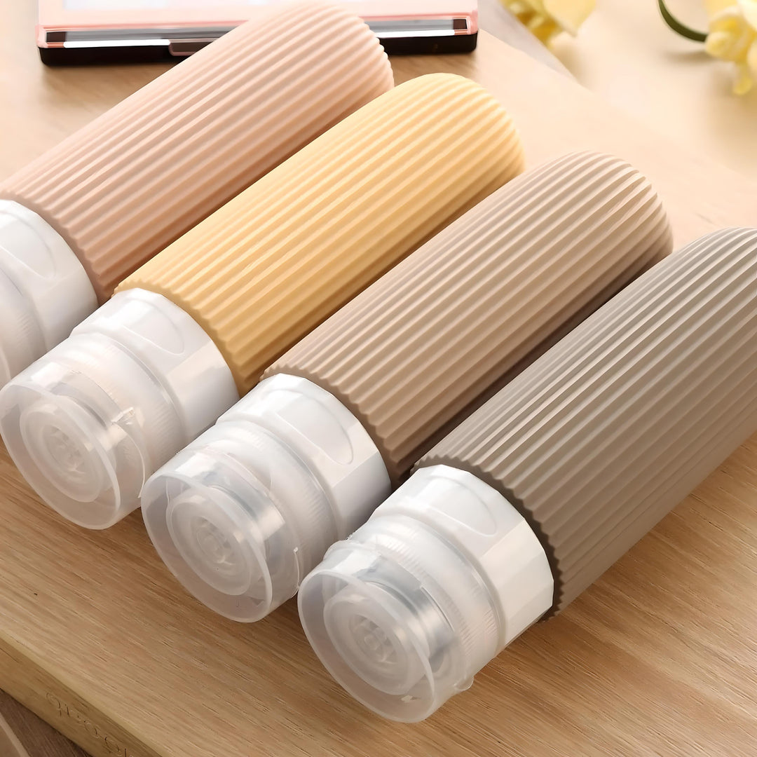 Quattro flaconi da viaggio in silicone colorati su tavola di legno, design pieghevole, ideali per shampoo e cosmetici. Accessori da viaggio pratici.