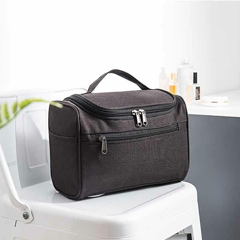 Borsa da toilette nera su sedia bianca, con zip multiple, ideale per viaggi. Design compatto, resistente all'acqua, perfetta per organizzare accessori.
